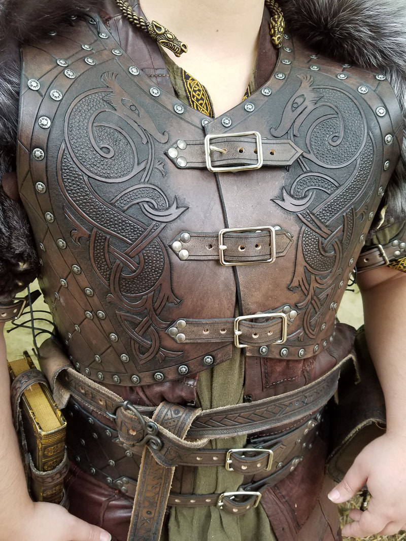 Close up of dark brown buckled breastplate with tooled Norse dragons.