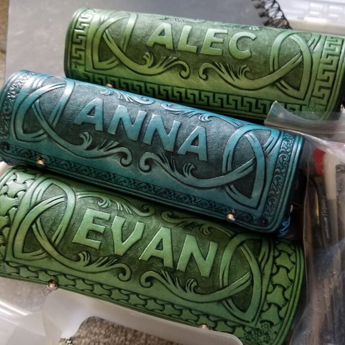Three cylindrical pencil holders, two green and one teal, with tooled names.